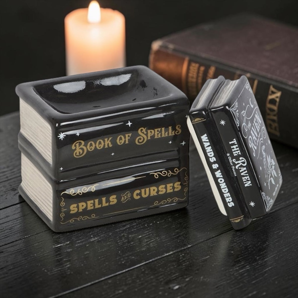 Keramische waxbrander vormgegeven als een zwarte stapel spreukenboeken met goudkleurige details en titels zoals 'Book of Spells' en 'The Raven', op een houten ondergrond.⁠